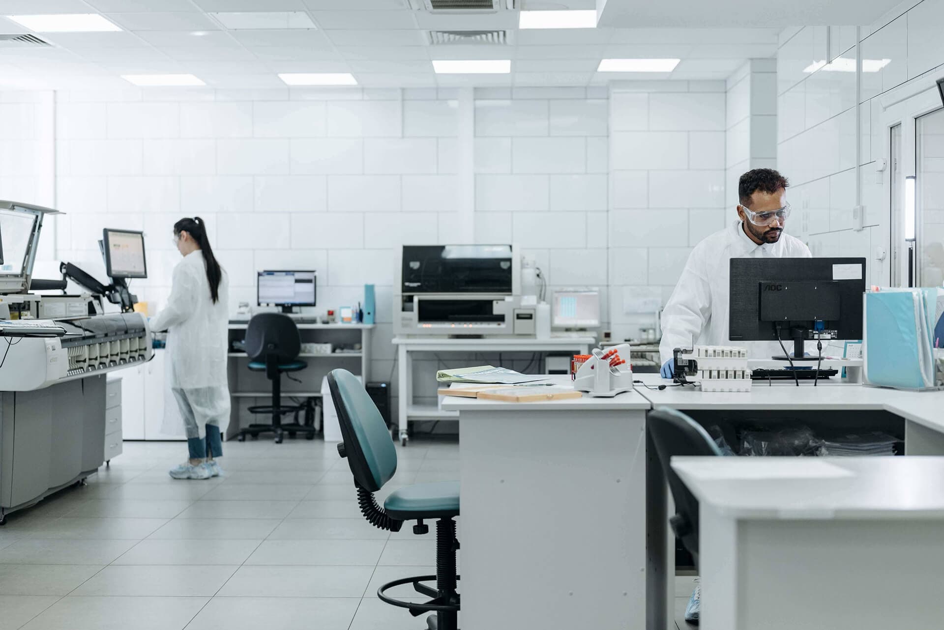Two analysts in laboratory coats working at benched analytical instruments