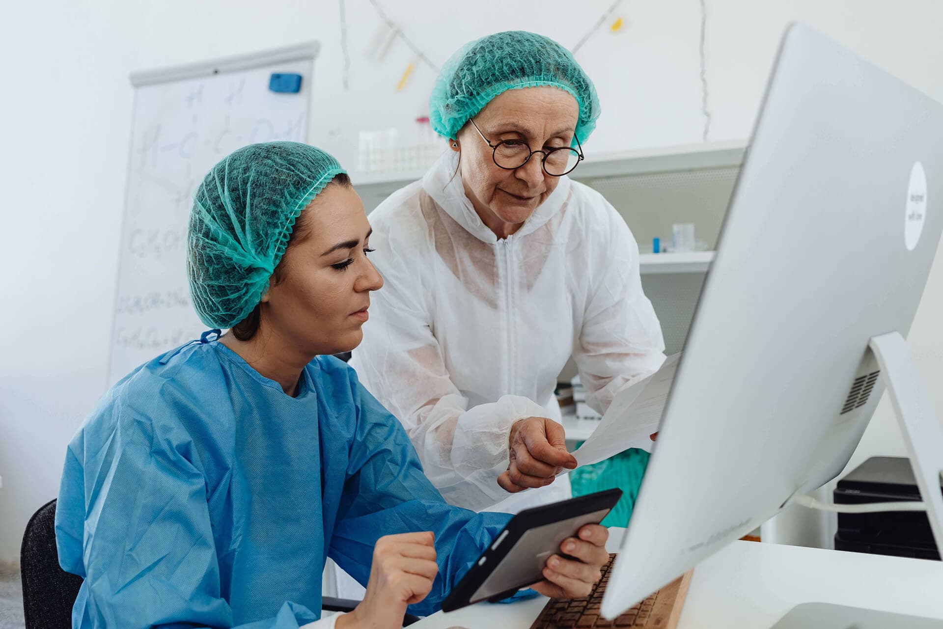 Two gowned staff reviewing a printed document together at a workstation